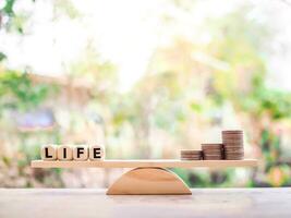 Wooden blocks with the word LIFE and stack of coins on balancing scale. The choice between life and money. photo