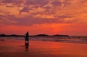 silueta de chico montando un bicicleta en el playa con dramático cielo foto