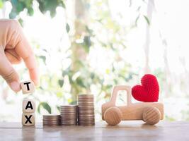 Close up hand holding wooden block with word TAX, wooden toy car, stack of coins. The concept of paying tax for car. photo