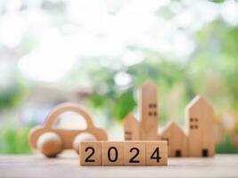 Close up of wooden block number 2024 with miniature house and toy car background. The concept of Transportation insurance, Property investment, House mortgage, Real estste in new year 2024 photo