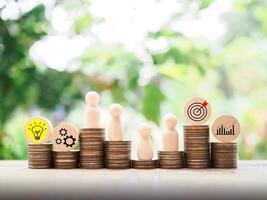 Wooden human figure standing on stack of coins with  business strategy icons, Action plan and business process management concept. photo