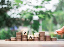 Close up hand putting coin in stack of coins, Wooden blocks with the word VAT. The concept of save money for paying vat in the future photo