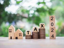 Wooden blocks with the word TAX on stack of coins, number 2024 and miniature house. The concept of Property investment, House mortgage, Real estste. photo