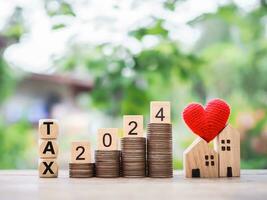 Wooden blocks with the word TAX 2024 on stack of coins and miniature house. The concept of Property investment, House mortgage, Real estste. photo