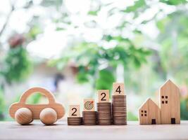 Wooden block with number 2024 on stack of coins, wooden toy car and miniature house. The concept of saving money  for car and house in new year 2024 photo