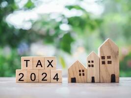 Wooden blocks with the word TAX 2024 and miniature house. The concept of Property investment, House mortgage, Real estste. photo