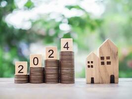 Wooden blocks with number 2024 on stack of coins and miniature house. The concept of Property investment, House mortgage, Real estste. photo