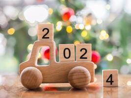 de madera bloquear número 2024 en de madera juguete coche con Navidad ligero bokeh antecedentes. alegre Navidad y contento nuevo año, el concepto de coche en nuevo año 2024. foto