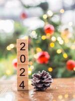 Wooden block number 2024 and pinecones with Christmas light bokeh background. Merry Christmas and Happy New Year 2024 photo