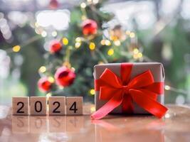 de madera bloquear número 2024 y regalo caja con Navidad ligero bokeh antecedentes. alegre Navidad y contento nuevo año 2024 foto