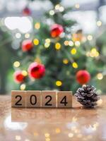 Wooden block number 2024 and pinecones with Christmas light bokeh background. Merry Christmas and Happy New Year 2024 photo