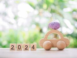 Wooden block with number 2024, Wooden toy car with Easter eggs for EASTER DAY concept. photo