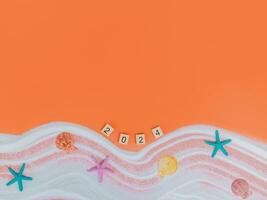 Wooden block with number 2024, seashells, starfish and white sand on orange background. Top view with copy space of summer background. The concept for summer of new year 2024 photo