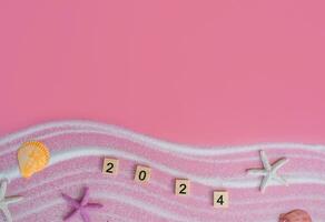 Wooden block with number 2024, seashells, starfish and white sand on pink background. Top view with copy space of summer background. The concept for summer of new year 2024 photo