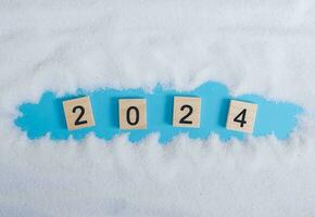 Wooden block with number 2024 and white sand on blue background. Top view with copy space of summer background. The concept for summer of new year 2024 photo