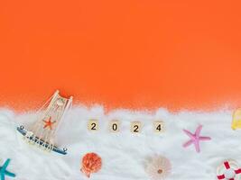 Wooden block with number 2024, seashells, starfish and white sand on orange background. Top view with copy space of summer background. The concept for summer of new year 2024 photo