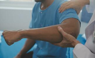 médico o fisioterapeuta trabajando examinando tratando lesionado brazo de atleta masculino paciente, extensión y ejercicio, haciendo el rehabilitación terapia dolor en clínica. foto