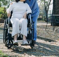 Asian young woman nurse at nursing home take care disabled senior man. Caregiver doctor serve physical therapy for older elderly patient to exercise and practice walking on walker or cane at backyard. photo