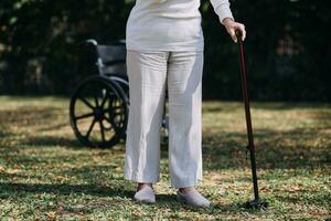 Asian young woman nurse at nursing home take care disabled senior man. Caregiver doctor serve physical therapy for older elderly patient to exercise and practice walking on walker or cane at backyard. photo