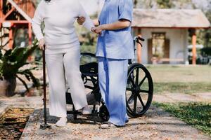 Asian young woman nurse at nursing home take care disabled senior man. Caregiver doctor serve physical therapy for older elderly patient to exercise and practice walking on walker or cane at backyard. photo