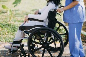 Asian young woman nurse at nursing home take care disabled senior man. Caregiver doctor serve physical therapy for older elderly patient to exercise and practice walking on walker or cane at backyard. photo