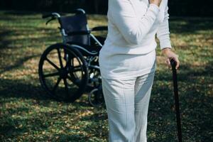 Asian young woman nurse at nursing home take care disabled senior man. Caregiver doctor serve physical therapy for older elderly patient to exercise and practice walking on walker or cane at backyard. photo