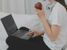 Efficient Young Millennial Girl Sitting on a Bed in the Morning, Uses Laptop Computer and Eats Croissants and Drinks Coffee for Breakfast photo