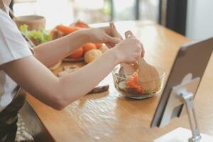 Delicious fruit and vegetables on a table and woman cooking. Housewife is cutting green cucumbers on a wooden board for making fresh salad in the kitchen. photo