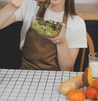 Delicious fruit and vegetables on a table and woman cooking. Housewife is cutting green cucumbers on a wooden board for making fresh salad in the kitchen. photo