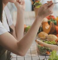 Delicious fruit and vegetables on a table and woman cooking. Housewife is cutting green cucumbers on a wooden board for making fresh salad in the kitchen. photo