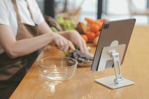 Delicious fruit and vegetables on a table and woman cooking. Housewife is cutting green cucumbers on a wooden board for making fresh salad in the kitchen. photo