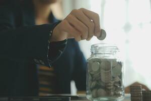 saving money and accounting concept. business man putting coin insert to jar and make acounting book for finance management to investment and saving. photo