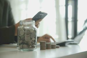 saving money and accounting concept. business man putting coin insert to jar and make acounting book for finance management to investment and saving. photo