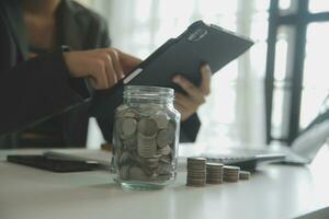 saving money and accounting concept. business man putting coin insert to jar and make acounting book for finance management to investment and saving. photo