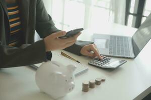 saving money and accounting concept. business man putting coin insert to jar and make acounting book for finance management to investment and saving. photo