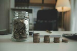 saving money and accounting concept. business man putting coin insert to jar and make acounting book for finance management to investment and saving. photo