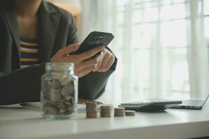 saving money and accounting concept. business man putting coin insert to jar and make acounting book for finance management to investment and saving. photo