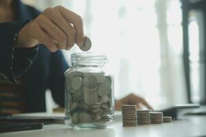 saving money and accounting concept. business man putting coin insert to jar and make acounting book for finance management to investment and saving. photo