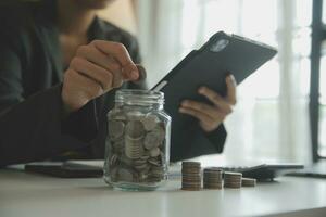 saving money and accounting concept. business man putting coin insert to jar and make acounting book for finance management to investment and saving. photo