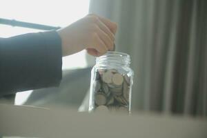 saving money and accounting concept. business man putting coin insert to jar and make acounting book for finance management to investment and saving. photo