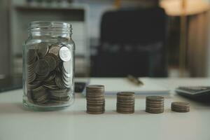 saving money and accounting concept. business man putting coin insert to jar and make acounting book for finance management to investment and saving. photo