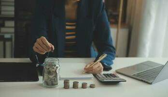 saving money and accounting concept. business man putting coin insert to jar and make acounting book for finance management to investment and saving. photo