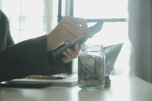 saving money and accounting concept. business man putting coin insert to jar and make acounting book for finance management to investment and saving. photo