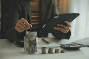 saving money and accounting concept. business man putting coin insert to jar and make acounting book for finance management to investment and saving. photo