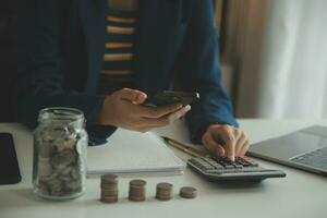 saving money and accounting concept. business man putting coin insert to jar and make acounting book for finance management to investment and saving. photo