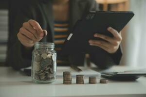 ahorro dinero y contabilidad concepto. negocio hombre poniendo moneda insertar a tarro y hacer contabilidad libro para Finanzas administración a inversión y ahorro. foto