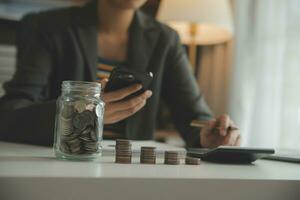 ahorro dinero y contabilidad concepto. negocio hombre poniendo moneda insertar a tarro y hacer contabilidad libro para Finanzas administración a inversión y ahorro. foto