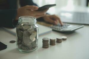 saving money and accounting concept. business man putting coin insert to jar and make acounting book for finance management to investment and saving. photo