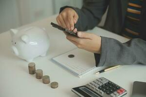 saving money and accounting concept. business man putting coin insert to jar and make acounting book for finance management to investment and saving. photo