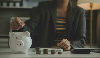 saving money and accounting concept. business man putting coin insert to jar and make acounting book for finance management to investment and saving. photo